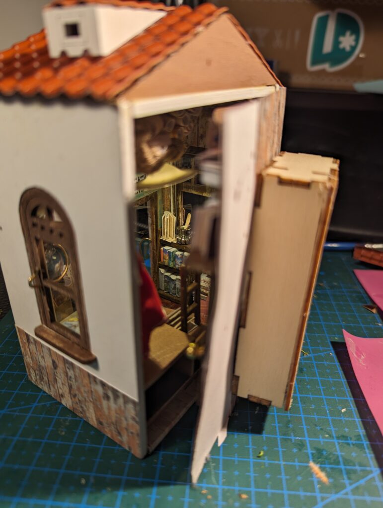 We see that the back of the miniature opens, and glimpse at books lining the walls. There's a hint of a red coat on a hook, and several maps and sea charts on the ceiling. 